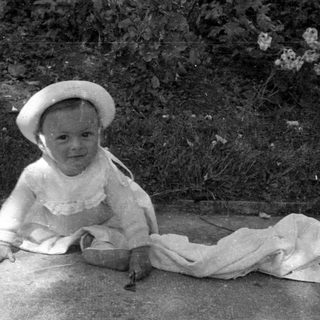 Young child in a hat sitting outdoors.