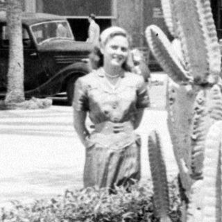 Woman standing by a cactus with vintage cars.