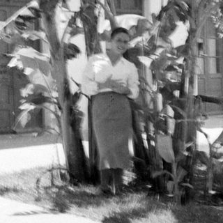Woman standing among tropical plants before a white building.