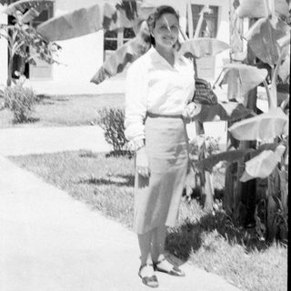 Woman in blouse and skirt standing by tropical plants.