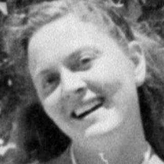 Woman in a blazer standing before a tree.