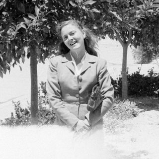 Woman in a blazer standing before a tree.