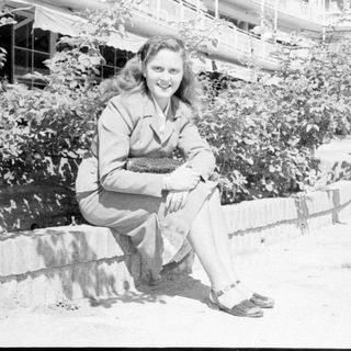 Woman in a suit sitting outdoors by foliage.