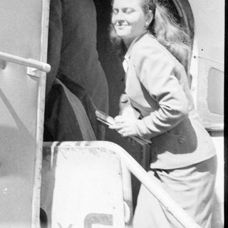 Woman in a suit standing in a vehicle doorway.