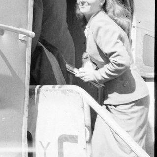 Woman in a suit standing in a vehicle doorway.