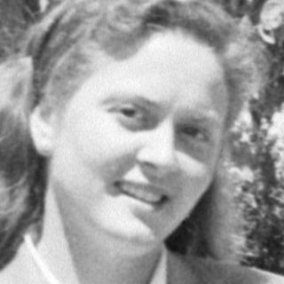 Woman in a tailored suit standing before a tree.