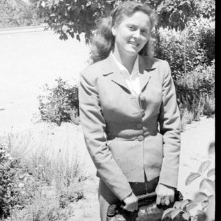 Woman in a tailored suit standing before a tree.