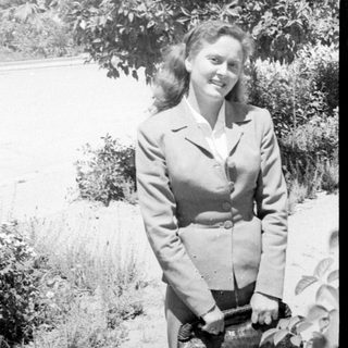 Woman in a tailored suit standing before a tree.