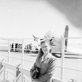 Woman standing before a propeller airplane on a tarmac.