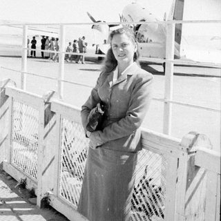 Woman standing before a propeller airplane on a tarmac.
