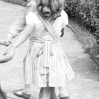 Children holding hands in a garden by a house.