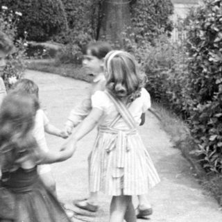 Children holding hands in a garden by a house.