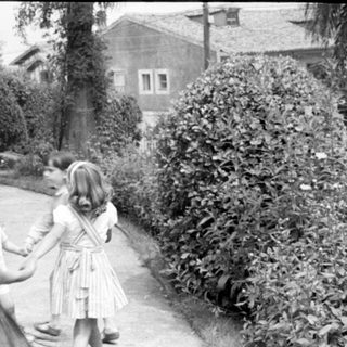Children holding hands in a garden by a house.