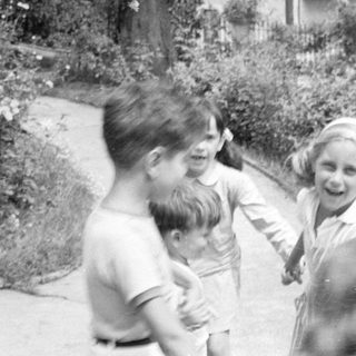 Three children on a garden path near a building.