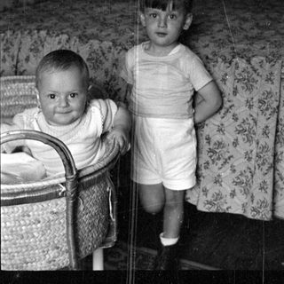 Two young children in a bedroom with a bassinet.