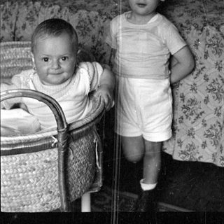 Two young children in a bedroom with a bassinet.