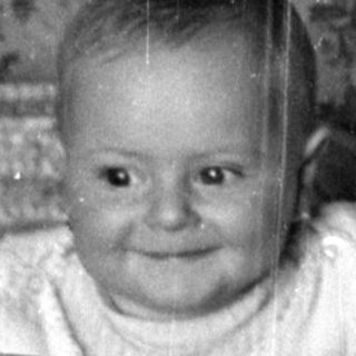 Infant in bassinet and toddler standing on bed.