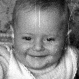 Infant smiling in a woven wicker bassinet.
