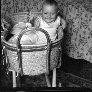 Infant smiling in a woven wicker bassinet.