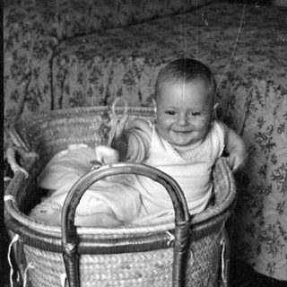 Infant smiling in a woven wicker bassinet.