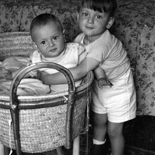 Young child standing beside a baby in a bassinet.