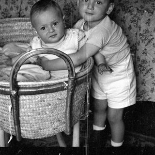 Young child standing beside a baby in a bassinet.