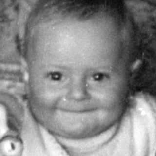 Infant sitting in a wicker bassinet indoors.