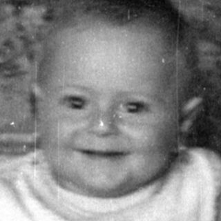 Infant sitting in a woven wicker bassinet.