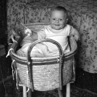 Infant sitting in a woven wicker bassinet.