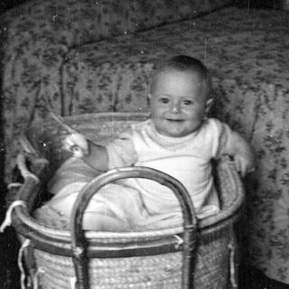 Infant sitting in a woven wicker bassinet.