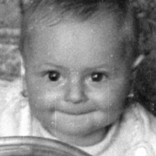 Infant sitting in a wicker bassinet.
