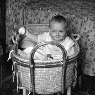 Infant sitting in a wicker bassinet.