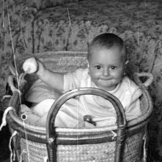 Infant sitting in a wicker bassinet.