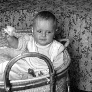 Infant sitting in a woven bassinet indoors.
