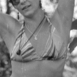 Woman in striped bikini posing by garden trellis.