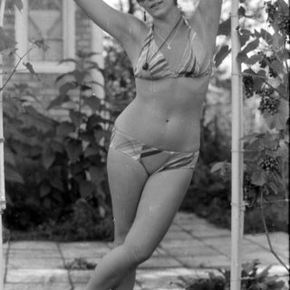 Woman in striped bikini posing by garden trellis.