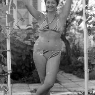 Woman in striped swimsuit reclining under a trellis.