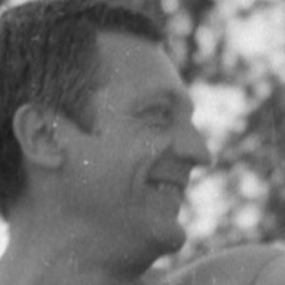 Shirtless man standing under a garden trellis.