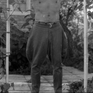 Shirtless man standing under a garden trellis.