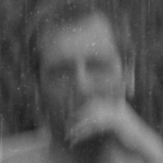 Shirtless man sitting in a chair under an umbrella.