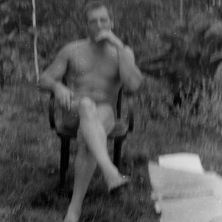 Shirtless man sitting in a chair under an umbrella.