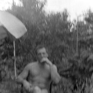 Shirtless man sitting in a chair under an umbrella.