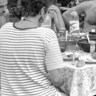 Outdoor gathering with people around a lace-covered table.
