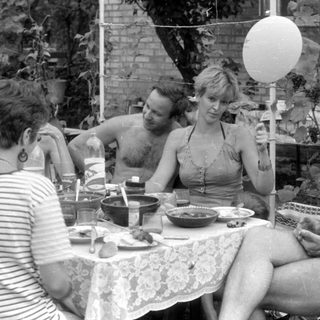 Outdoor gathering with people around a lace-covered table.