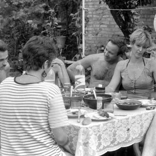 Outdoor gathering with people around a lace-covered table.