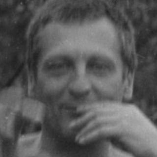 Shirtless man with a glass sitting outdoors.