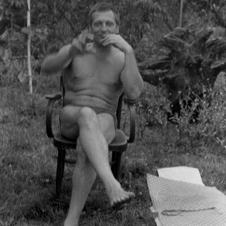 Shirtless man with a glass sitting outdoors.