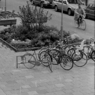 City street with stone building and parked bicycles.
