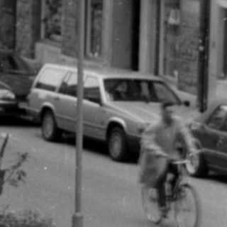 City street with stone building and parked bicycles.