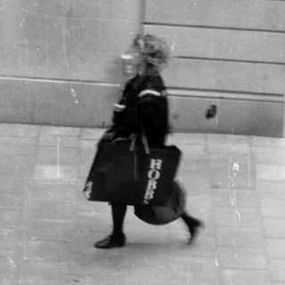 Person carrying bags walking past a stone building.